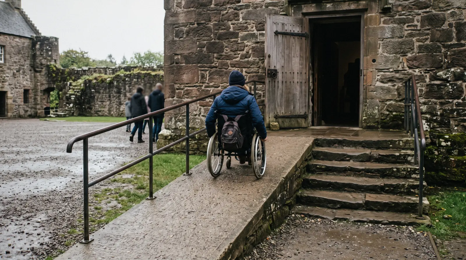 A wheelchair user on the smooth tarmac esplanade below the castle rock on a bright grey morning, the kind of surface Edinburgh accessibility depends on