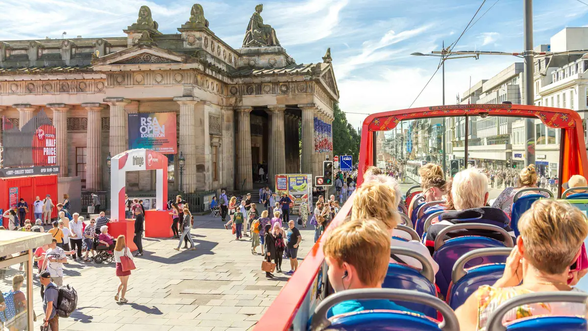 Open-top sightseeing bus passing the Palace of Holyroodhouse on the Royal Edinburgh attractions and bus ticket